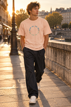 Man wearing the 1TIME2 Dream Big organic tee in Fraiche Peche, walking along a riverside street at sunset