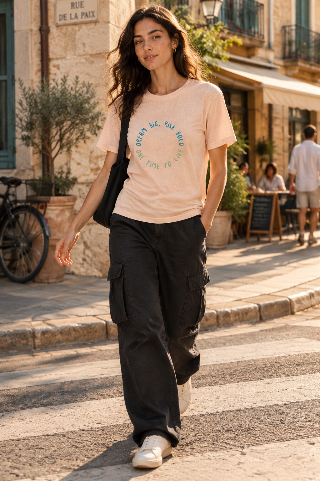 Woman wearing the 1TIME2 Dream Big organic tee in Fraiche Peche with black cargo pants on a sunny street