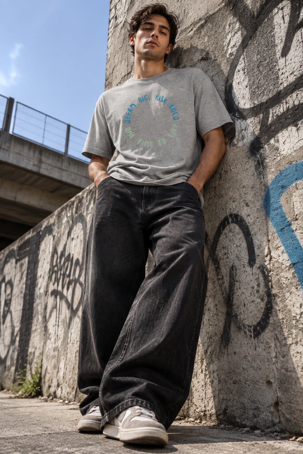 Man wearing the 1TIME2 Dream Big organic tee in Heather Grey, leaning against a graffiti wall